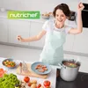 A woman is happily cooking in a modern kitchen, with ingredients and a large pot on the stove. Produktbild-Vorschau