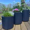 Three dark gray planters filled with various plants are arranged on a wooden deck. Podgląd zdjęcia produktu