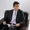 A man in a suit sits in a chair reading a magazine while wearing a Bluetooth headset. Produktbild-Vorschau