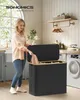 A woman is putting laundry into a SONGMICS laundry basket in a laundry room. Produktbild-Vorschau