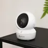 A white EZVIZ camera sits on a black table with a green leaf in the background. Podgląd zdjęcia produktu