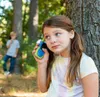 Two children in a forest setting, one holding a walkie-talkie to their ear. Produktbild-Vorschau