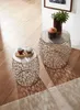 Two decorative side tables with intricate metal bases and silver tops, placed on a wooden floor next to a rug. One table has a red cup and a small pastry on it, while the other has a plant and a decorative pot. Produktbild-Vorschau
