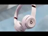 Close-up shot of white Beats Solo 4 wireless headphones with rose gold accents, against a blurred blue and gray background. Produktbild-Vorschau