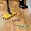 A yellow mop head is cleaning a wooden floor, with a pile of dirt in front of it. Two black boots are visible in the background. Produktbild-Vorschau
