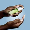 Hands holding a skincare product with cream dispensed onto a finger. Náhled obrázku produktu