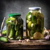 Two glass jars filled with pickles and garlic are displayed on a wooden surface. Podgląd zdjęcia produktu