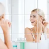 A woman is putting on earrings in front of a mirror, which is made up of multiple reflective tiles. Produktbild-Vorschau
