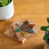 A wooden Chinese checkers board game with colorful marbles is placed on a wooden table, next to a potted plant. Produktbild-Vorschau