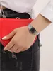 A woman's hand wearing a silver watch and holding a red purse. Produktbild-Vorschau