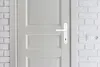 A close-up view of a white door with a white door handle, next to a white brick wall with electrical outlets. Produktbild-Vorschau