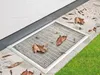 A metal grate cover for a basement window well, with fallen leaves scattered on it and the surrounding patio and grass. Produktbild-Vorschau
