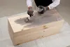 A person is shown applying a gray stain to a wooden block. Voir les images du produit