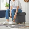 A person is sitting on a storage ottoman and tying their shoes. Náhled obrázku produktu