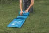 A person is kneeling on grass and rolling up a blue air mattress. Podgląd zdjęcia produktu
