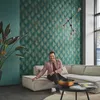 A man is sitting on a sectional sofa in a living room with a patterned wallpaper. Podgląd zdjęcia produktu