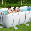 A family enjoying a rectangular above-ground swimming pool in a grassy backyard. Produktbild-Vorschau