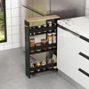 A narrow black kitchen cart with four shelves filled with jars and containers is placed next to a white kitchen cabinet and a marble countertop. Podgląd zdjęcia produktu