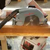 A person is using a MAFELL MKS 130 Ec circular saw to cut a piece of wood, with a vacuum hose attached to the saw for dust collection. Another MAFELL tool is visible below. Produktbild-Vorschau