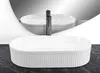 A white oval sink with a fluted exterior sits on a dark marble countertop, reflected in a mirror behind it. Anteprima dell’immagine prodotto
