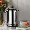 A chrome kettle sits on a countertop next to a vase of flowers and a cup of coffee. Anteprima dell’immagine prodotto