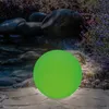 A glowing green sphere sits on a stone path next to a water feature and lavender plants. Produktbild-Vorschau
