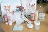 A collection of small cosmetic and bath products arranged on a wooden surface, with decorative boxes in the background featuring woodland animal illustrations. Produktbild-Vorschau