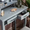 A close-up view of a gray vanity table with makeup and jewelry on it, and an open drawer showing makeup. Produktbild-Vorschau