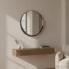 A round mirror hangs above a floating wooden console table with decorative items and books. Produktbild-Vorschau