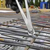 A person wearing black gloves is using a pair of pliers to tie rebar on a construction site. Produktbild-Vorschau