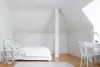 A minimalist white bedroom with a bed, desk, and chair. Produktbild-Vorschau
