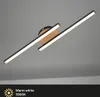 A modern LED ceiling light with two angled light bars mounted on a circular wooden base, set against a plain gray background. Produktbild-Vorschau