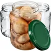 Three glass jars, one filled with preserved mushrooms and a green lid, are arranged on a white background. Produktbild-Vorschau