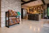 A modern kitchen with a brick wall and concrete floor, featuring a beverage crate rack in the foreground and a kitchen island with stools in the background. Produktbild-Vorschau