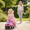 A woman walks behind a young child riding a pink toy car in a garden. Produktbild-Vorschau