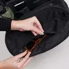 A person is reaching into a black bag and pulling out a pair of sunglasses. Produktbild-Vorschau