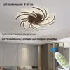 A modern LED ceiling light fixture with a swirling design, mounted on a white ceiling. The image also shows a remote control and a section of a room's interior. Anteprima dell’immagine prodotto
