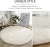 A round, fluffy white rug is shown in a living room setting, with a sofa, plant, and artwork. Produktbild-Vorschau
