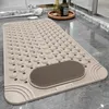 A beige bath mat with textured nubs and a scrubbing area is placed on a tiled bathroom floor next to a shower. Produktbild-Vorschau