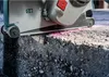 A close-up of a power tool cutting into a rough, dark material, with pink dust visible. Voir les images du produit