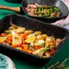 A baking tray filled with roasted vegetables and a pan with bacon and asparagus in the background. Produktbild-Vorschau