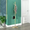 A gold tree-shaped coat rack with a plaid shirt and a black handbag hanging on it, placed in a room with a green wall and a white door. Produktbild-Vorschau