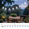 A string of solar-powered globe lights illuminates a patio deck at dusk, with a table and chairs visible. Produktbild-Vorschau