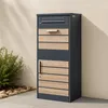 A modern mailbox with a wood-look finish is mounted on a textured wall next to a small bush and rocks. Anteprima dell’immagine prodotto