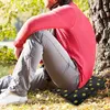 A person sitting on the ground next to a tree, using a portable seat cushion. Produktbild-Vorschau