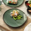 A close-up of a green plate with spring rolls and edamame, set on a wooden table. Produktbild-Vorschau