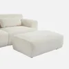 A cream-colored bouclé upholstered ottoman is placed in front of a matching sofa section, against a white background. Produktbild-Vorschau