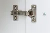 A close-up view of a cabinet hinge attached to white cabinet doors. Produktbild-Vorschau