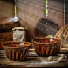 Two brown ceramic baking molds are placed on a rustic wooden table, with a bag of flour and some dried herbs in the background. Voir les images du produit