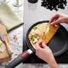 A person is folding a crepe in a pan on a stovetop, with ingredients like pears and nuts nearby. Produktbild-Vorschau